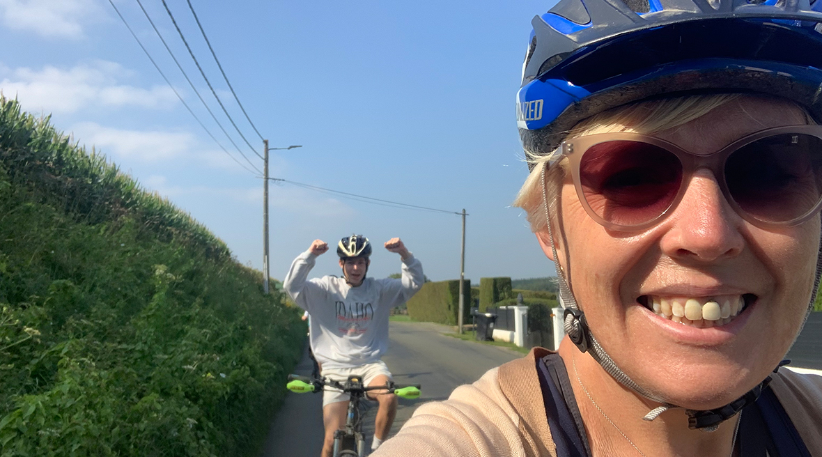 Smiling cyclist takes a picture of her teenage son cycling behind her and punching the air in joy